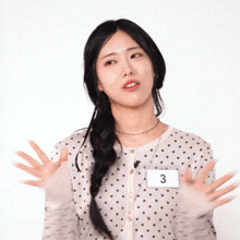 a woman wearing a polka dot sweater and a name tag with the number 3 on it is making a funny face .