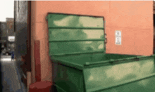 a green dumpster is sitting on the side of a building with the door open