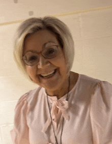 a woman wearing glasses and a pink blouse smiles for the camera