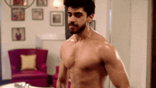 a shirtless man stands in front of a pink chair in a living room