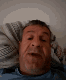a man with a beard is laying in bed with his head on a pillow and making a funny face .
