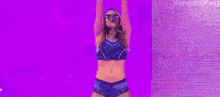 a woman is standing on a stage with her arms in the air and a purple background .
