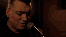 a man is singing into a microphone with his eyes closed