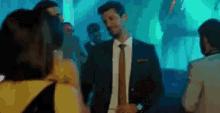 a man in a suit and tie is standing in front of a crowd of people at a party .