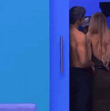 a shirtless man is standing next to a woman in a room with a blue wall .