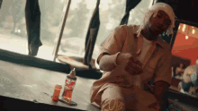 a man with a bandaged head sits on the floor next to a bottle that says coca cola