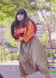 a woman wearing a mask and a long skirt is standing on a sidewalk