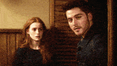 a man and a woman are standing next to each other in front of a wooden wall .