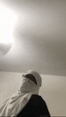a person wearing a white hijab and sunglasses is standing in a room .