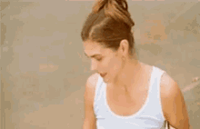 a woman in a white tank top is sitting on a beach .