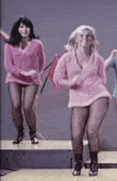 a group of women are dancing on a stage and one is wearing a pink sweater