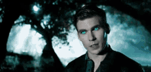 a man with blue eyes is standing under a tree in the dark .