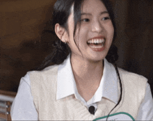 a girl wearing a white shirt and a sweater vest is smiling