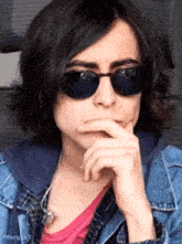 a young man wearing sunglasses and a denim jacket is making a funny face .