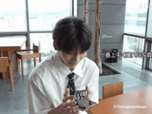 a young man in a white shirt and tie is looking at a cell phone with chinese writing on it