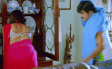 a woman in a red saree is standing next to a man in a blue shirt in a living room