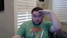 a man wearing a green zelda shirt holds his hand to his head