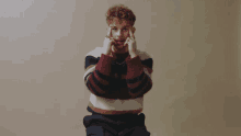 a man wearing a striped sweater is making a face with his hands