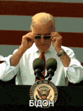 a man adjusts his sunglasses in front of the president of the united states emblem