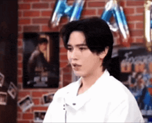a man in a white shirt is sitting in front of a brick wall and balloons .