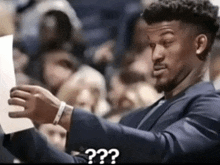 a man in a suit and tie is holding a piece of paper and says " ? " in the corner