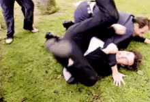 two men are wrestling in the grass and one of them is being kicked in the face .