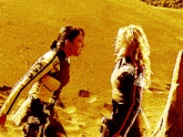 two women are standing in the sand with one wearing a jacket that says jvc on it
