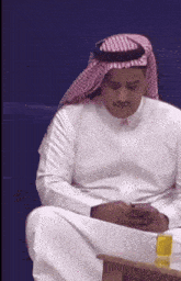 a man wearing a head scarf and a white shirt looks at his phone
