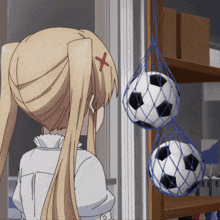 a girl with a red cross on her head looks at two soccer balls hanging from a shelf