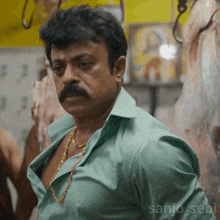 a man with a mustache is wearing a green shirt and gold chain