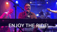 a man singing into a microphone on stage with the words enjoy the ride behind him