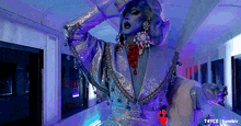 a drag queen in a silver and purple outfit is standing in a train car