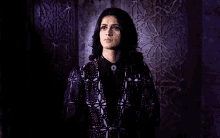 a woman is standing in a dark room wearing a purple jacket and black shirt .