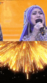 a woman is singing into a microphone with a fireworks display in the background
