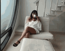 a woman sits in a chair drinking from a cup