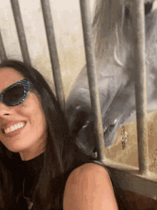 a woman wearing sunglasses is smiling in front of a horse in a cage