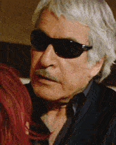 a man with gray hair and sunglasses looks at a woman