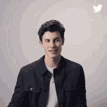 a young man in a black jacket is smiling in front of a twitter bird