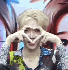 a man is making a heart shape with his hands over his eyes .