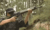 a man is holding a rifle in his right hand and aiming it at a target in the woods .