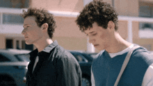 two young men with curly hair are standing next to each other in front of a building .