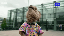 a dog wearing a colorful shirt is standing in front of a building that says bbc on it