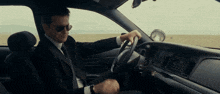 a man in a suit driving a car with sunglasses on
