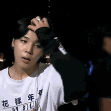 a young man wearing a white t-shirt with chinese writing on it is holding his head .
