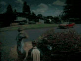 a red car is driving down a street with a group of people standing in front of it