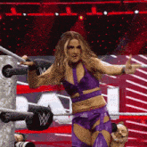 a woman in a purple outfit is standing in a wrestling ring with a w on the wall behind her