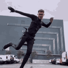 a man in a black suit is jumping in the air in a parking lot