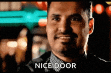 a man is smiling and saying `` nice door '' while standing in front of a neon sign .