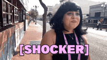 a woman is standing on a sidewalk with the word shocker written in pink letters