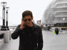 a man wearing sunglasses and a black jacket talks on a cell phone